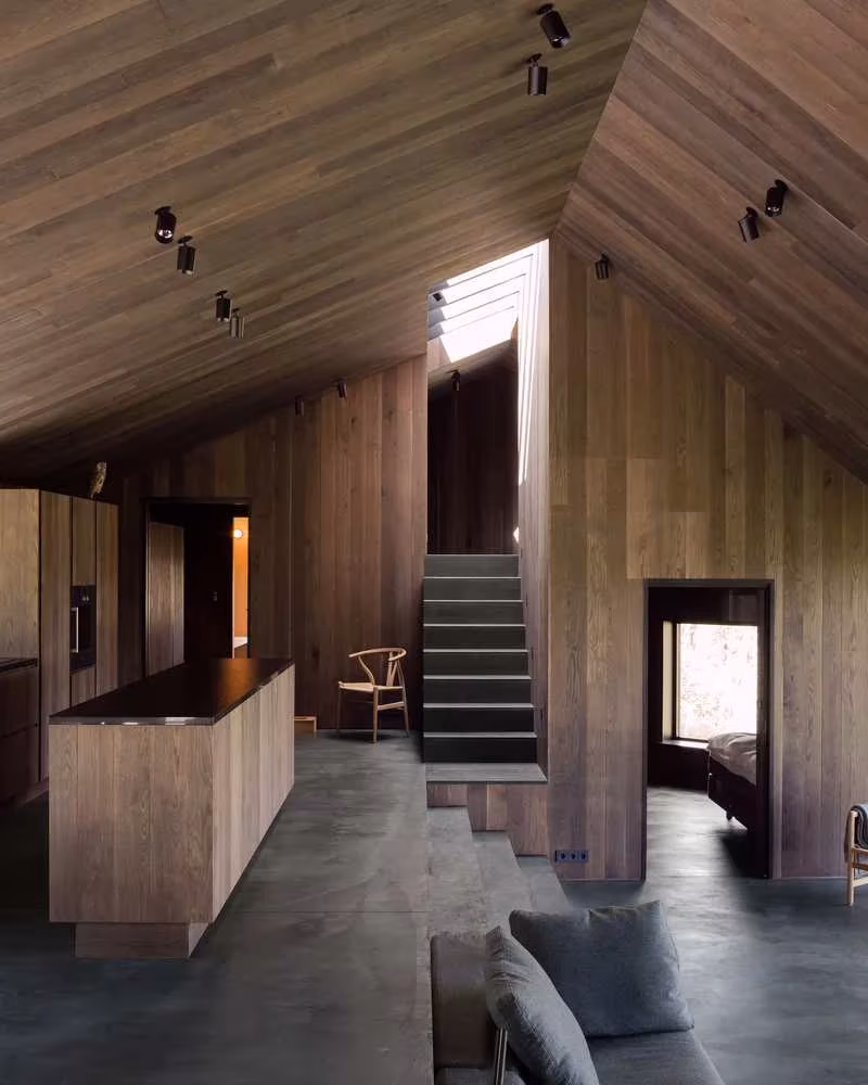 Interior de madera con cocina de isla, escalera y cubierta inclinada con lucernario en la Cabaña Geilo