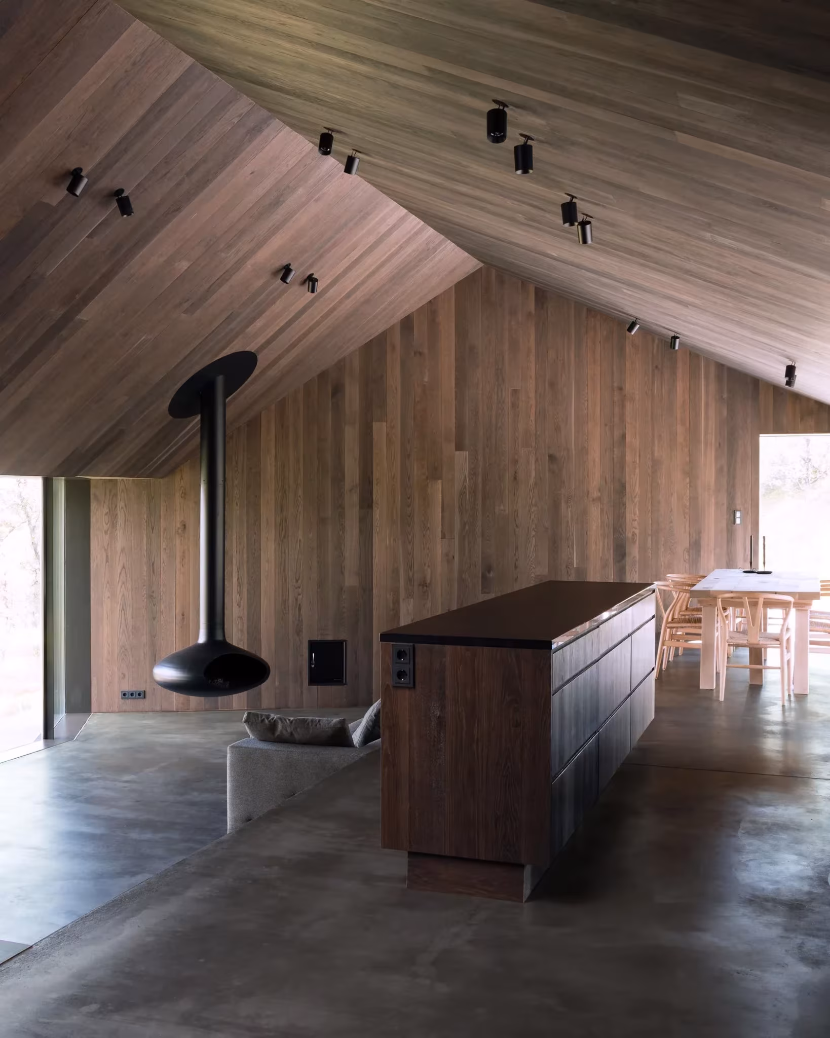 Salón de la Cabaña Geilo con chimenea suspendida, isla de cocina y paredes de madera bajo la cubierta inclinada