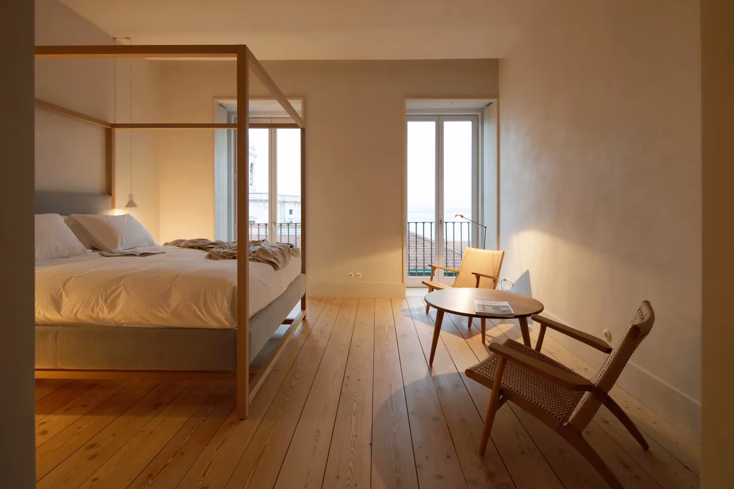 Dormitorio con cama de baldaquino de madera, suelo de tablones y butacas junto al balcón en el Santa Clara 1728