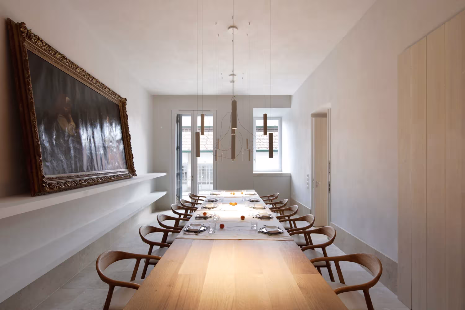 Comedor con larga mesa de madera y un cuadro antiguo en la pared en el hotel Santa Clara 1728 de Aires Mateus