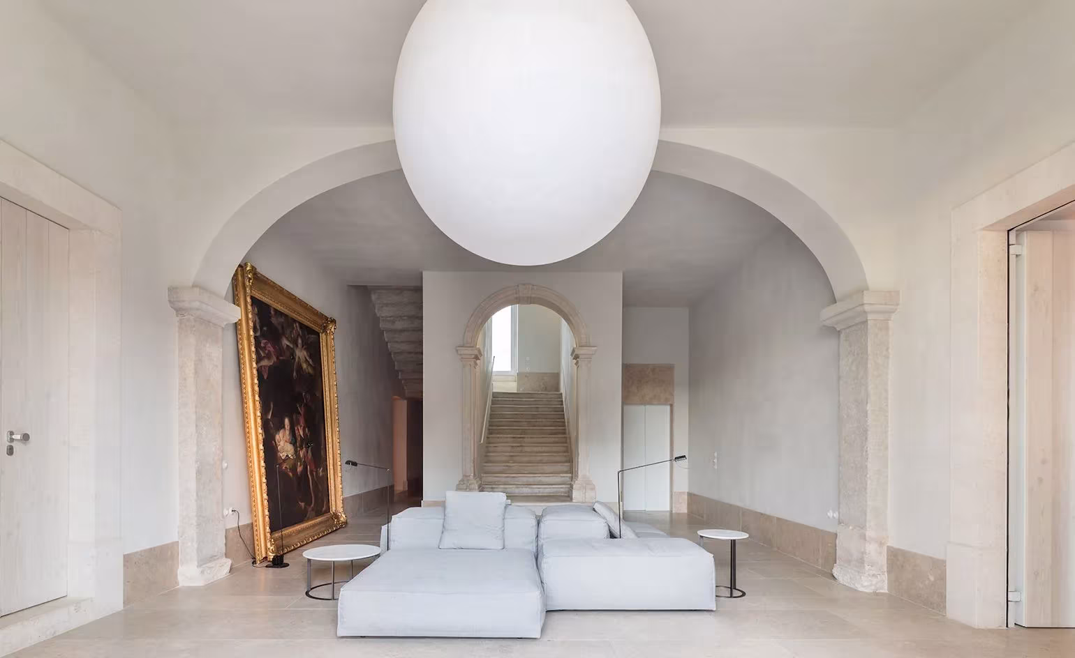 Sala con arcos, sofá blanco y gran lámpara esférica bajo pinturas antiguas en el hotel Santa Clara 1728