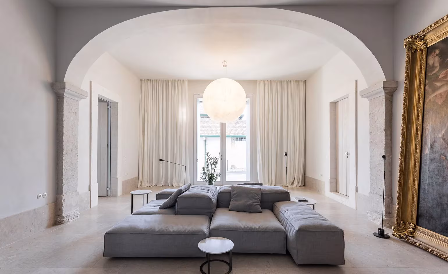 Salón con bóveda de arco, sofá gris modular y cortinas de lino ante el ventanal en el Santa Clara 1728 de Lisboa