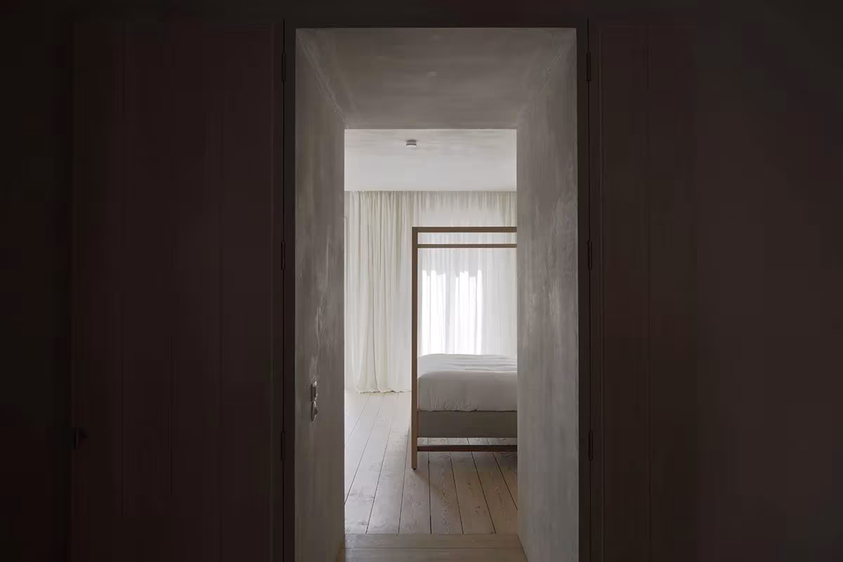 Vano de paredes oscuras que enmarca una habitación clara con cama de baldaquino en el Santa Clara 1728