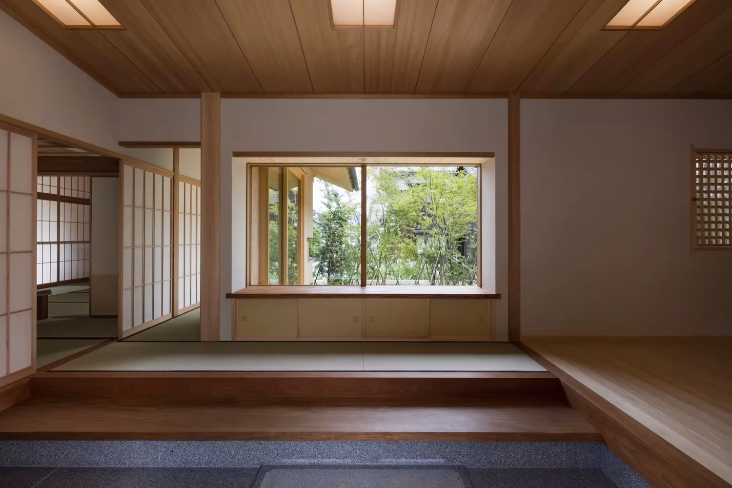 Sala de tatami con artesonado de madera y gran ventana al verde sobre un zócalo de piedra en la Casa Hiiragi