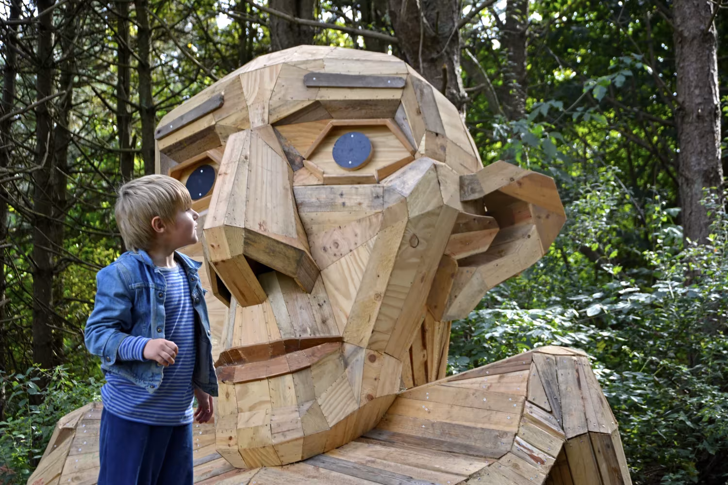 Gigante de madera reciclada de Thomas Dambo en un bosque de Copenhague, con un niño que observa su rostro tallado