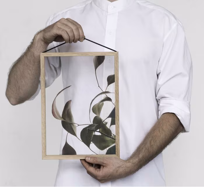 Persona con camisa blanca sosteniendo un marco de madera de roble con hojas verdes prensadas entre cristales