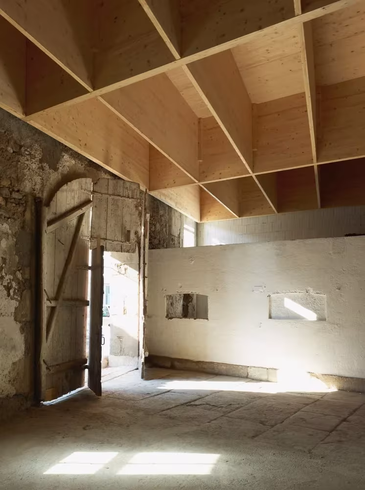 Sala del antiguo establo con muros de piedra, puerta de madera y forjado de vigas de abeto en Landecy