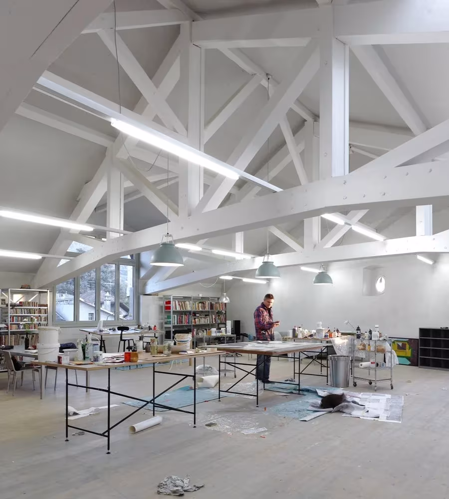 Estudio de artista con cerchas blancas de madera y mesas de trabajo en el establo reformado por Charles Pictet