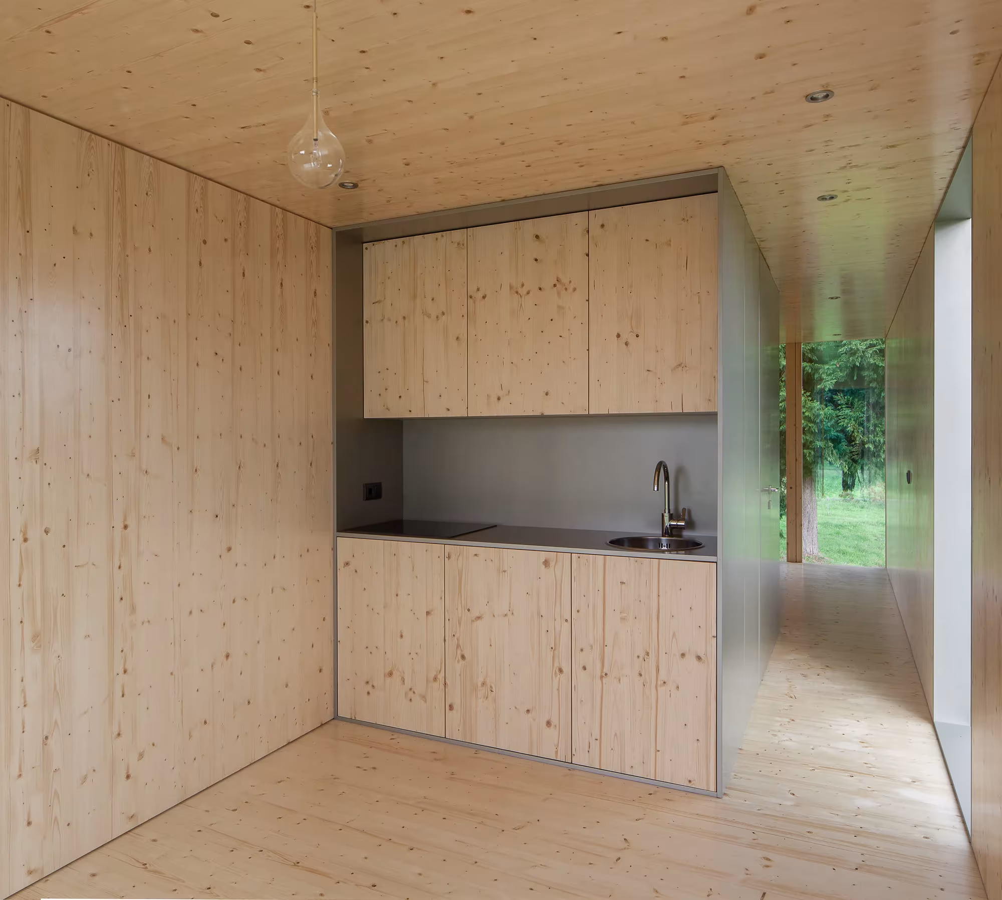 Cocina de madera de abeto con armarios altos y bajos y ventana al jardín en el interior de la MIMA Light