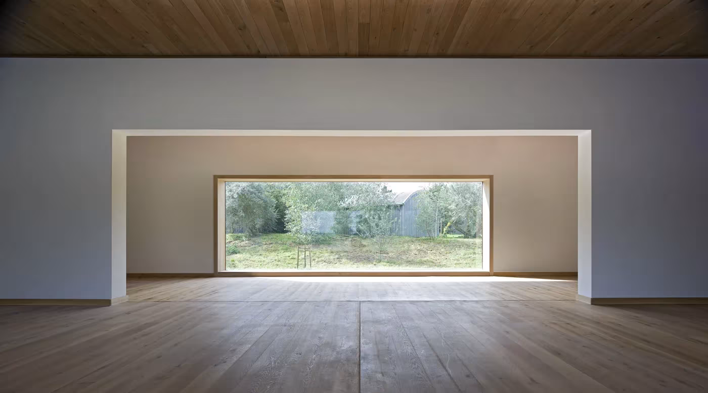 Sala diáfana con suelo de madera y gran ventana panorámica sobre el prado en el museo de Siza en Hombroich