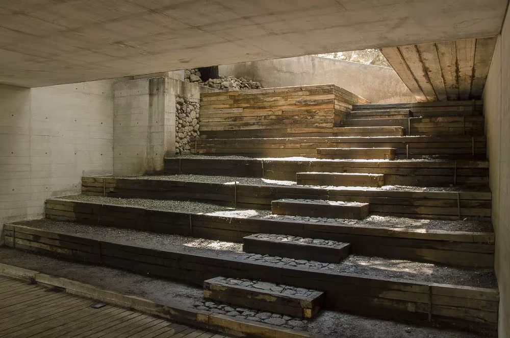 Escalinata de traviesas de madera y hormigón bajo el techo de la Casa BC, usada como gradas y asiento
