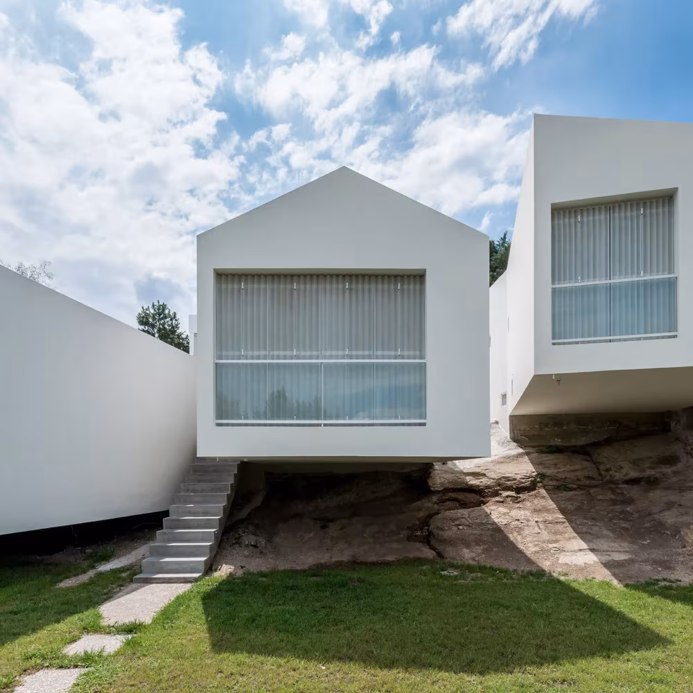 Frente de una de las casas blancas de 5 Casas sobre un afloramiento rocoso con escalera de acceso