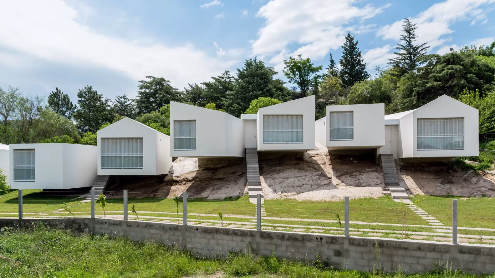 Casas blancas de tejado a dos aguas voladas sobre la roca con el jardín en primer plano, 5 Casas, Argentina