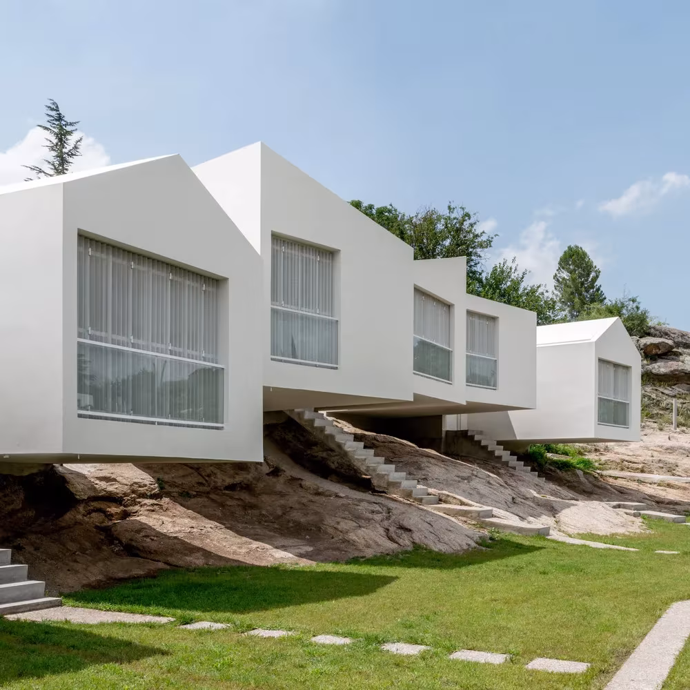 Fachadas blancas con ventanas apaisadas asomadas sobre la roca natural en el proyecto 5 Casas de Ciravegna