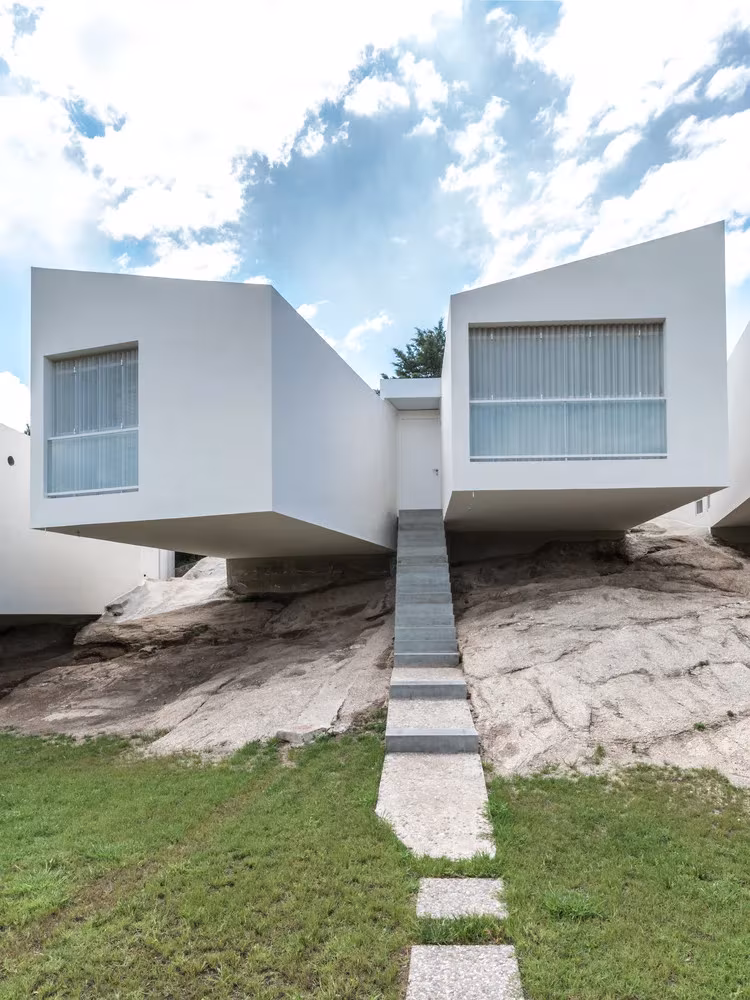 Dos volúmenes blancos en voladizo sobre la roca con una escalera de losas que baja al jardín en 5 Casas