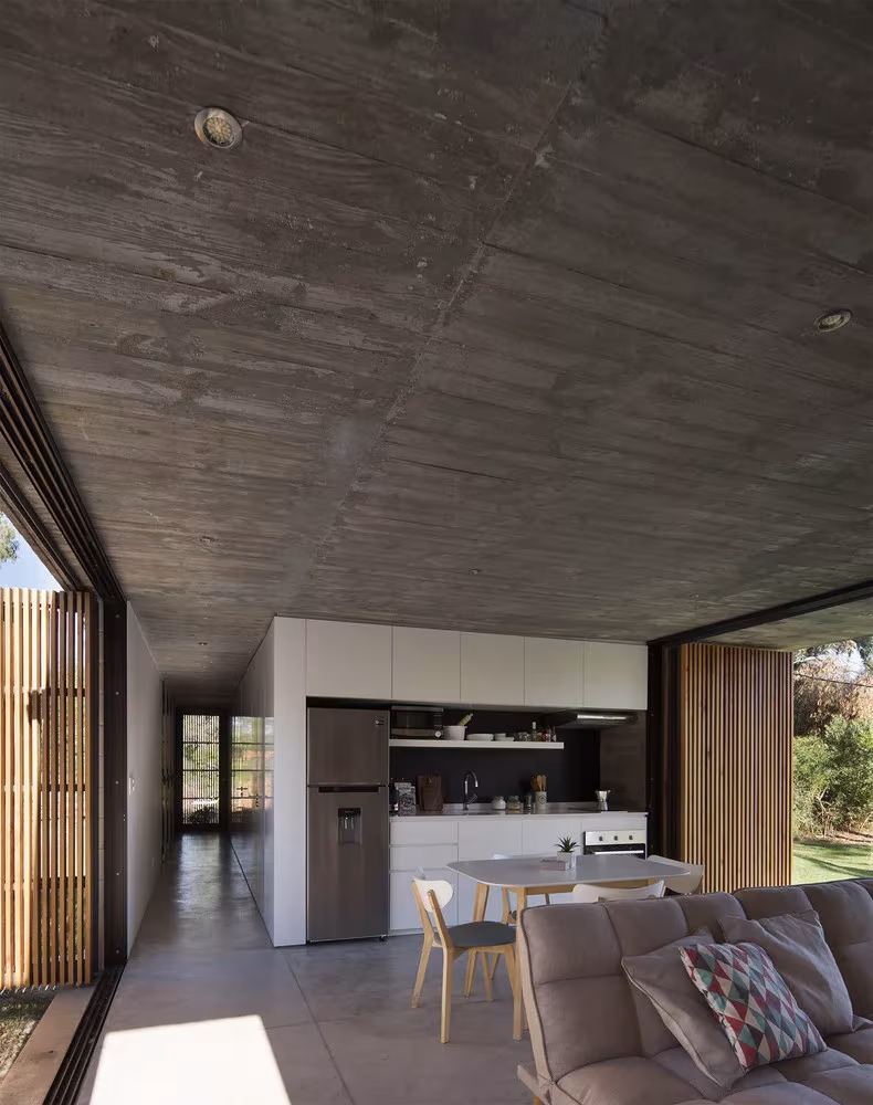 Cocina y salón de la Casa Marindia atravesados por una cristalera corredera con lamas de madera