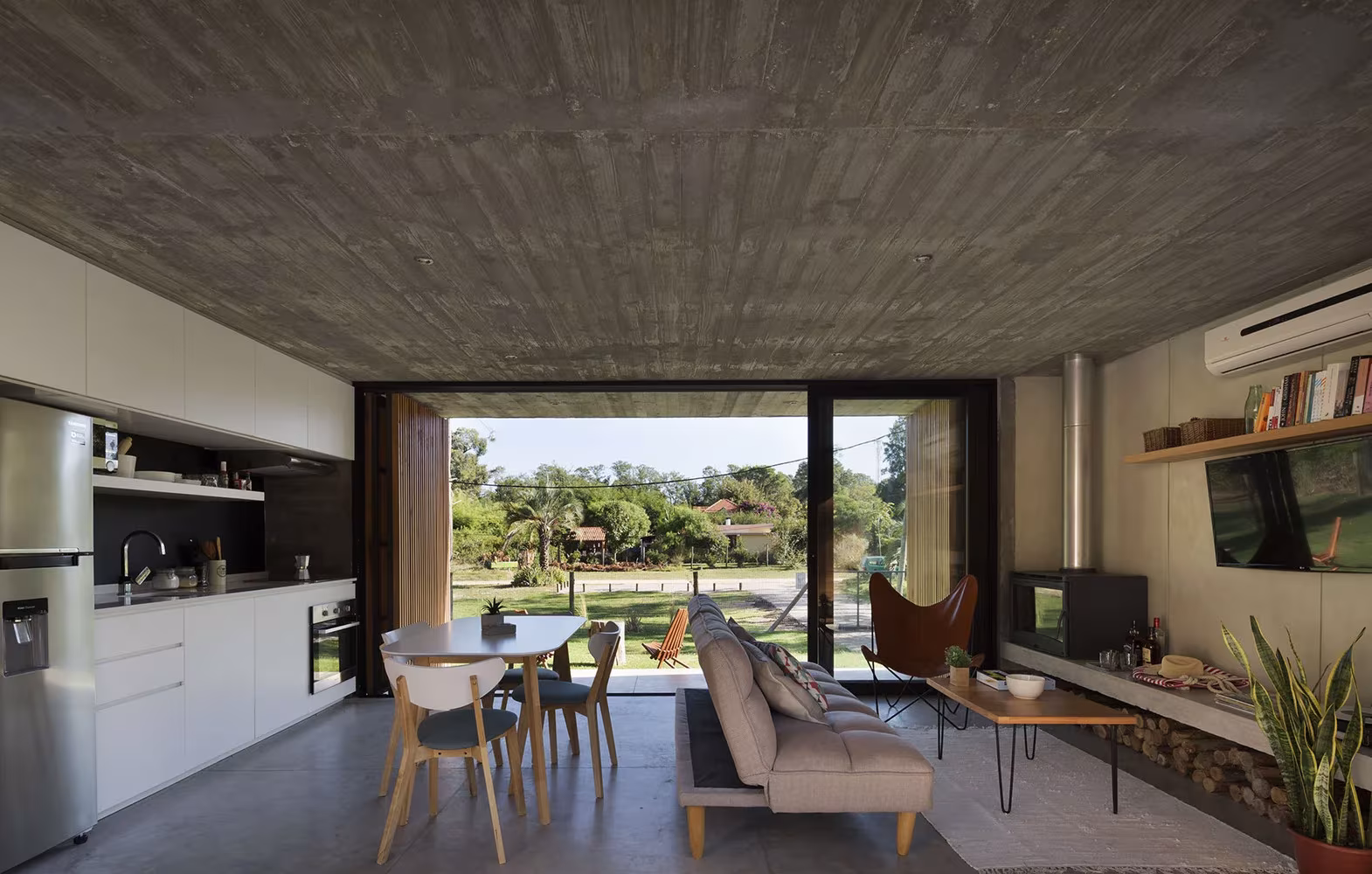 Cocina-comedor y sala de estar con techo de hormigón encofrado abiertos al jardín en la Casa Marindia