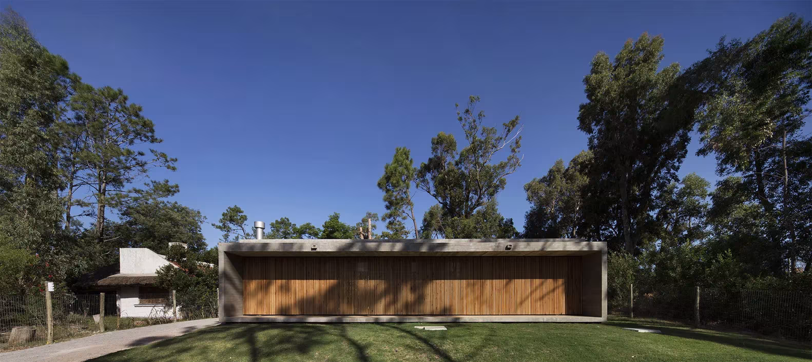 Casa Marindia de MASA Arquitectos, volumen bajo de hormigón con cierres de listones de madera entre los árboles