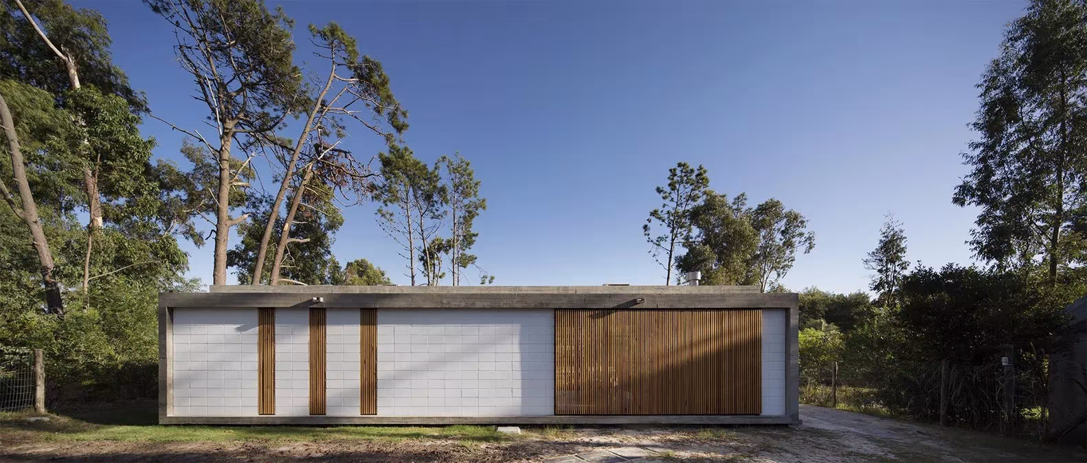 Alzado de la Casa Marindia con paños de bloque blanco y puertas de listones entre pinos inclinados