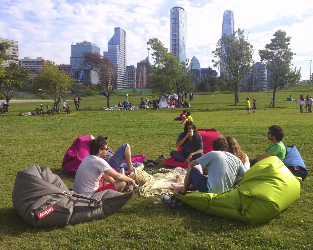 Grupo de amigos sentados sobre pufs de colores en un parque con rascacielos al fondo