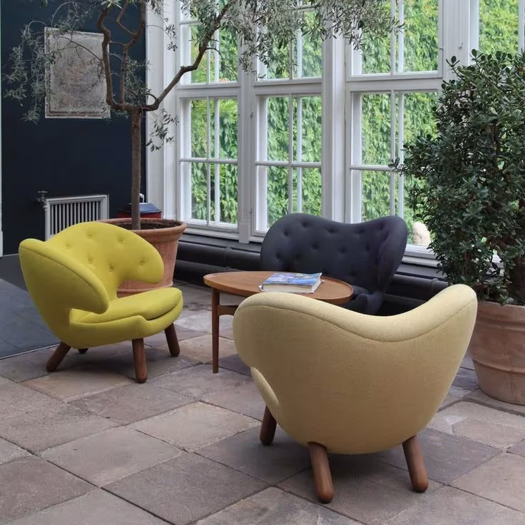 Tres butacas Pelícano de Finn Juhl en amarillo, mostaza y gris oscuro en un invernadero con olivos
