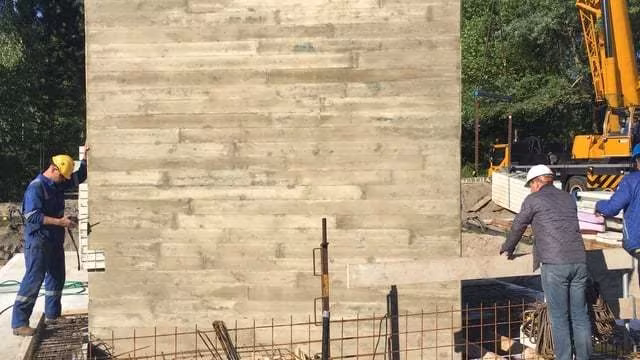 Obreros levantando un muro de hormigón con huella de encofrado de tablas durante la construcción de la Villa H