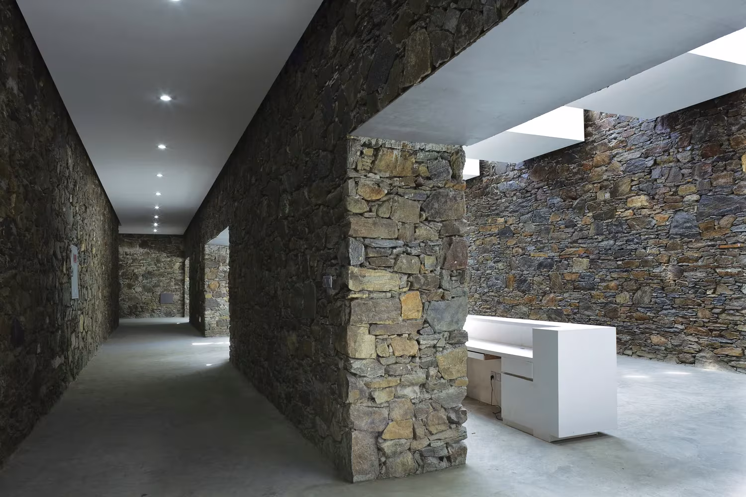Corredor entre muros de mampostería del centro de visitantes de Namchabawa, con luz natural y mostrador blanco