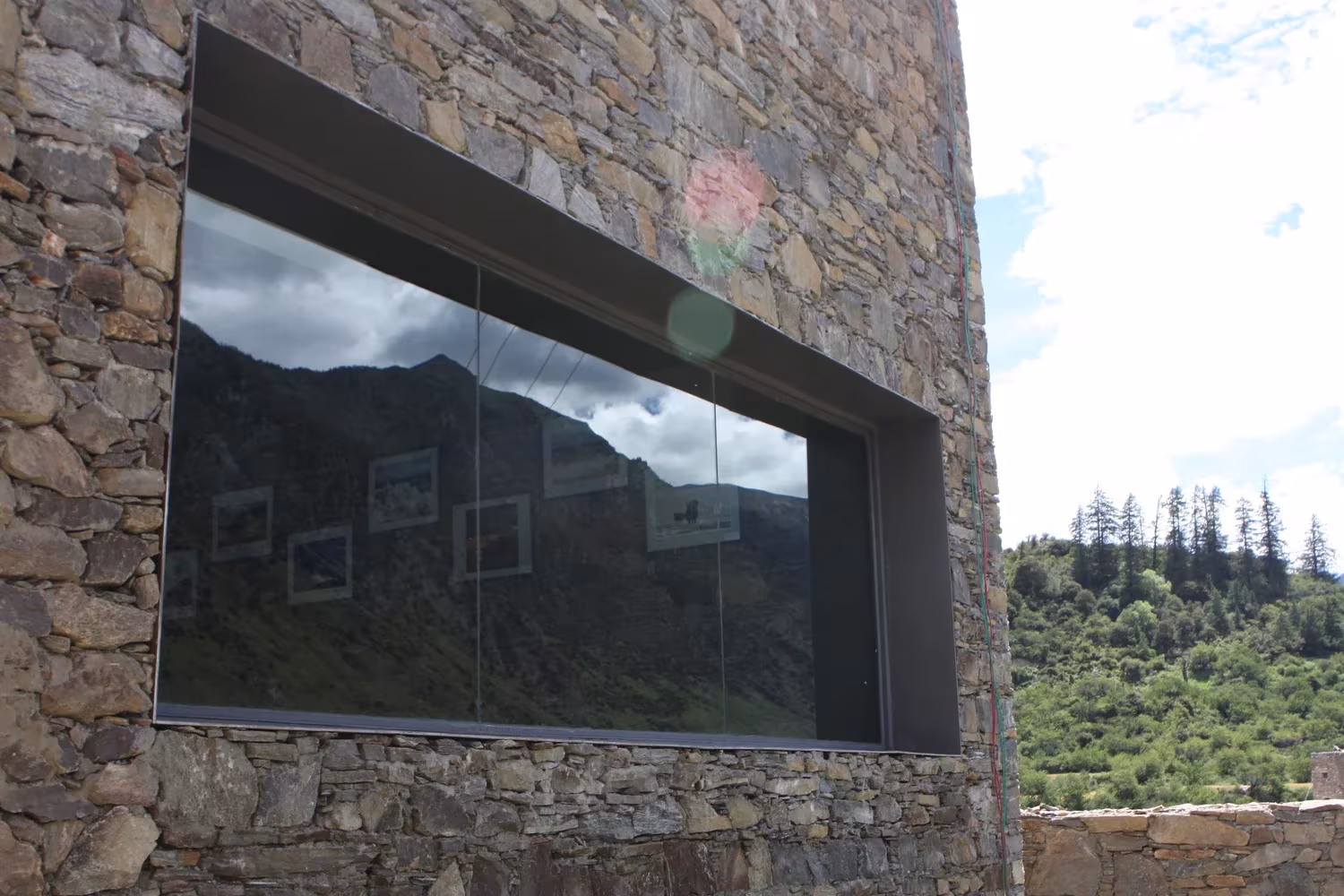 Gran ventana empotrada en el muro de piedra de Namchabawa, de standardarchitecture, con reflejo del paisaje tibetano
