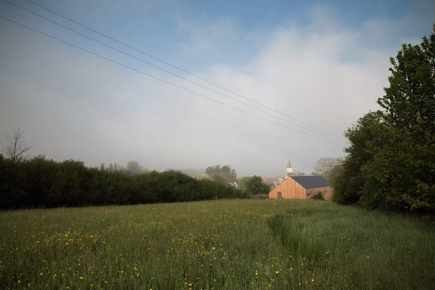 Pueblo y casa rural entre la bruma al fondo de una pradera florida en Borgoña-Franco Condado