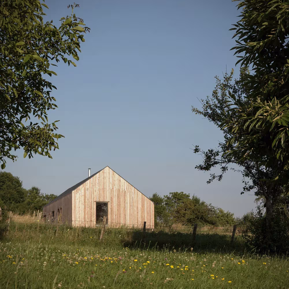 Fachada gablete de madera de la casa rural de Mathieu Noël entre árboles y flores silvestres en Francia