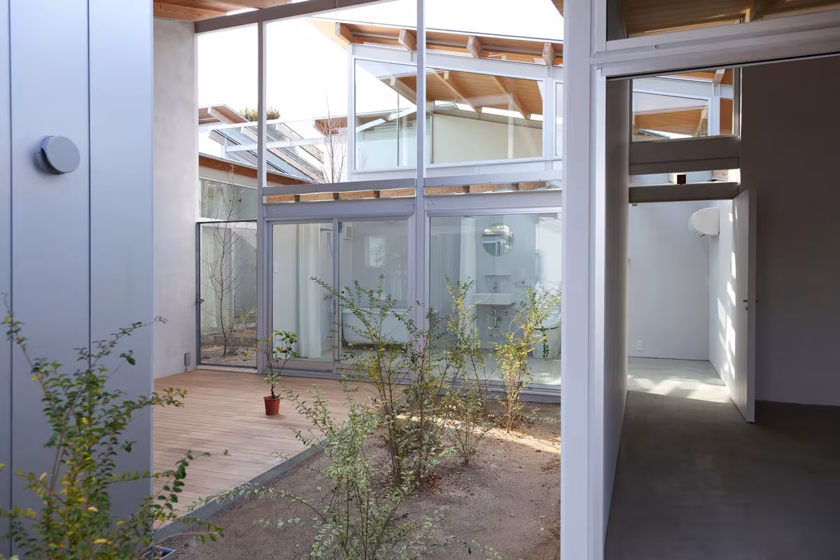 Patio interior con vegetación y cerramientos de vidrio entre viviendas de la Nishinoyama House de SANAA en Kioto