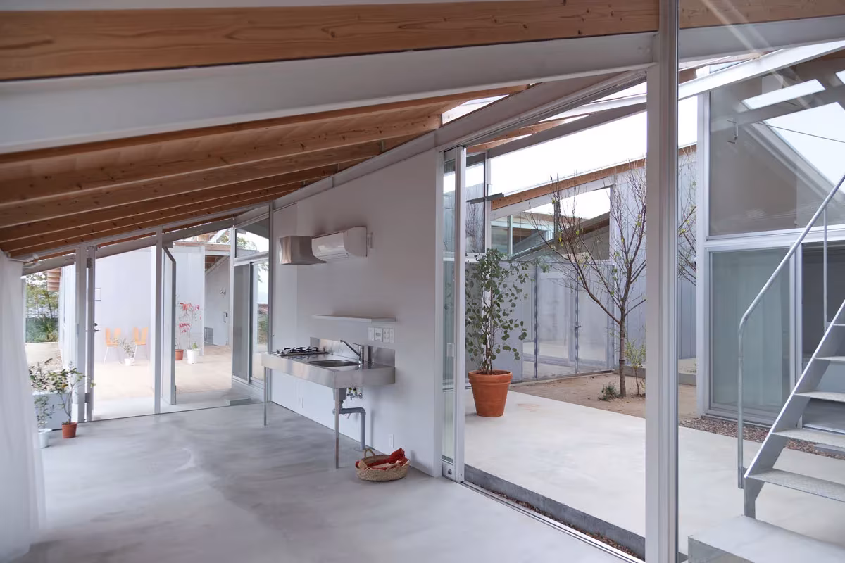 Interior de la Nishinoyama House con techo inclinado de madera, suelo de cemento y vidrio hacia el patio, SANAA