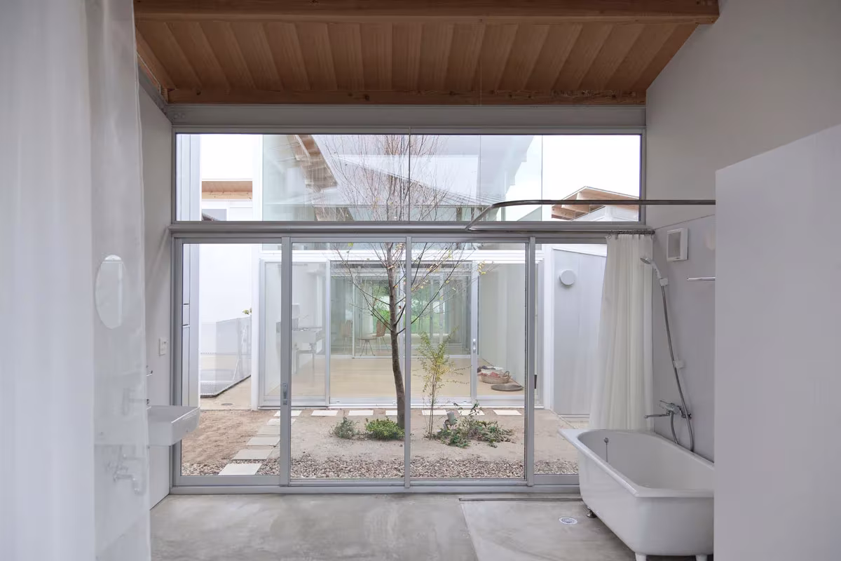 Bañera y cortina frente a un patio con árbol visto a través del vidrio en la Nishinoyama House de SANAA