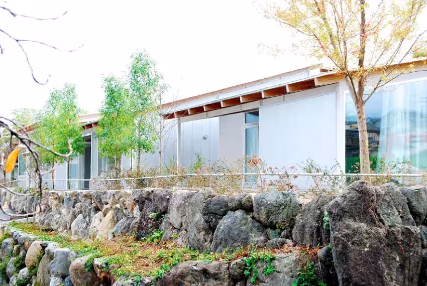 Cubierta ligera y fachada de vidrio de la Nishinoyama House sobre un muro de piedra con vegetación, Kioto