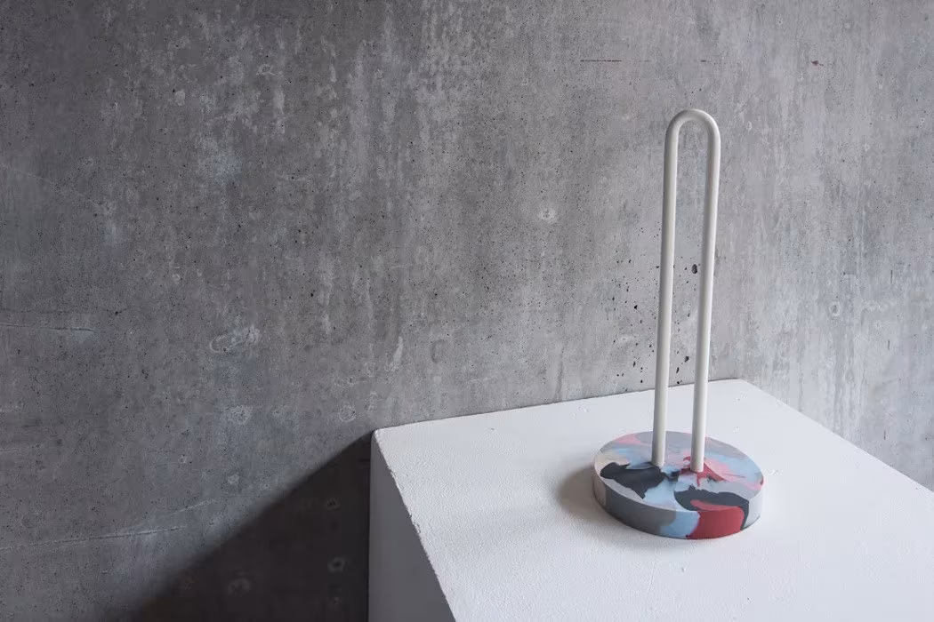 Portarrollos de varilla blanca con base jaspeada de la colección Beyond Local sobre un pedestal ante pared de cemento