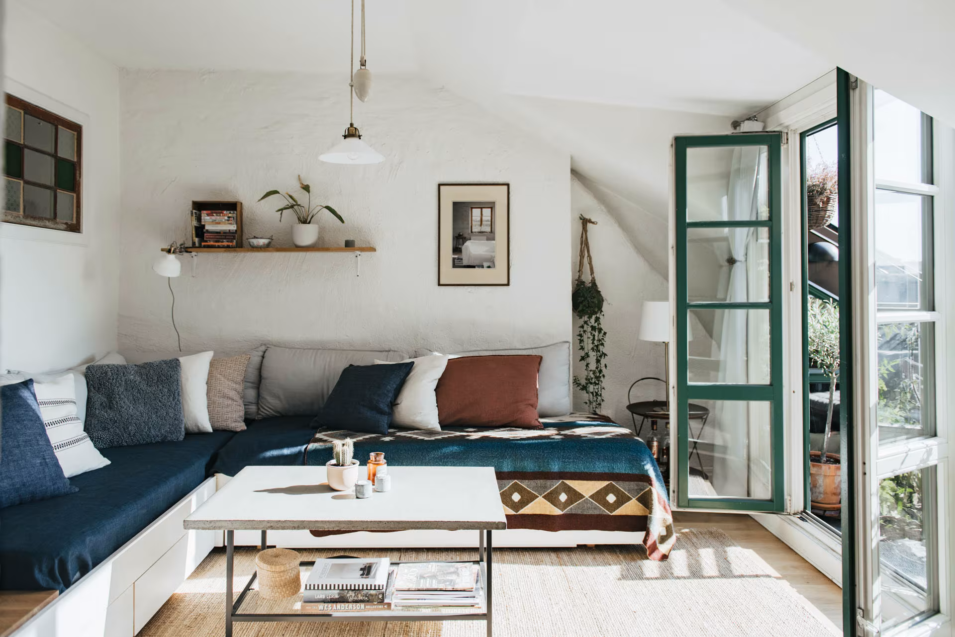 Salón con sofá en esquina azul, carpintería verde abierta y paredes blancas en un ambiente boho