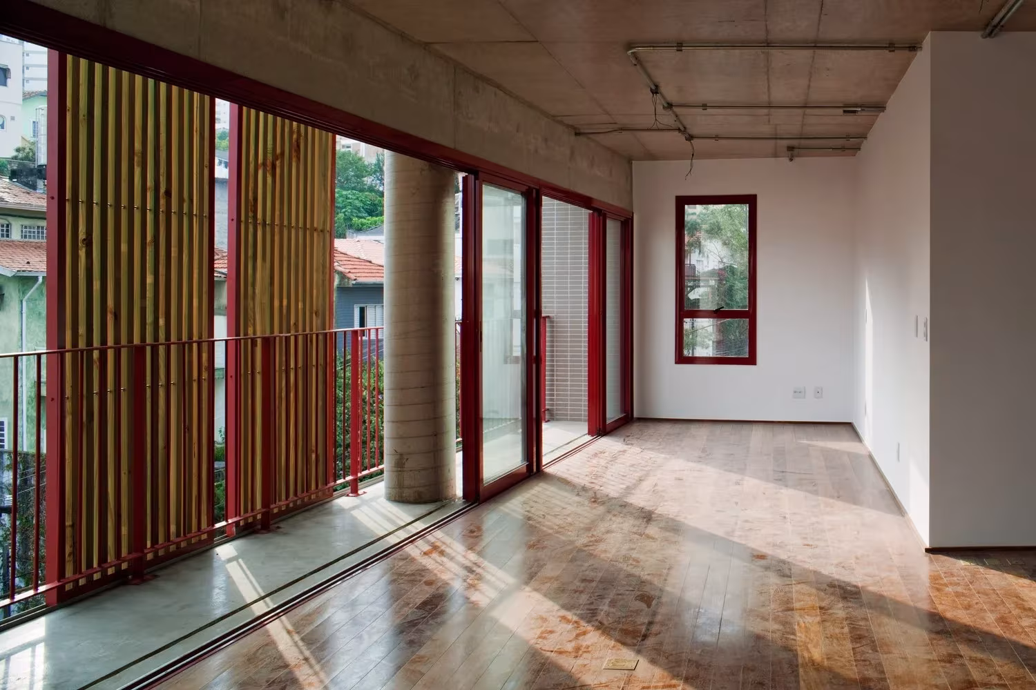 Vivienda diáfana con suelo de madera, carpintería roja y celosía de lamas hacia la ciudad en la Rua Simpatia