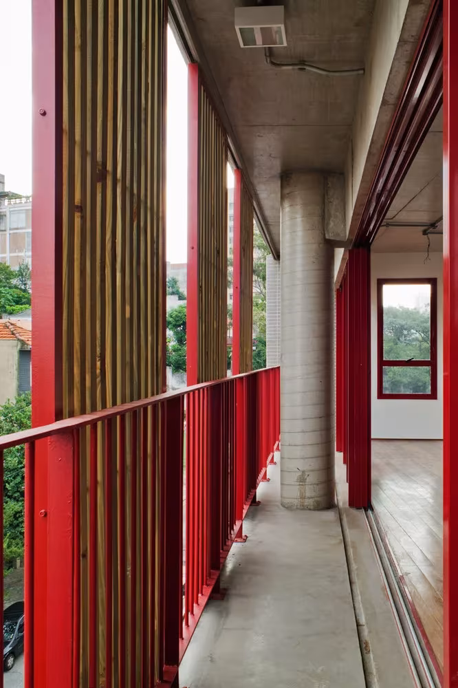 Balcón corrido con barandilla roja, lamas de madera y pilar de hormigón en el edificio de Grupo SP, São Paulo