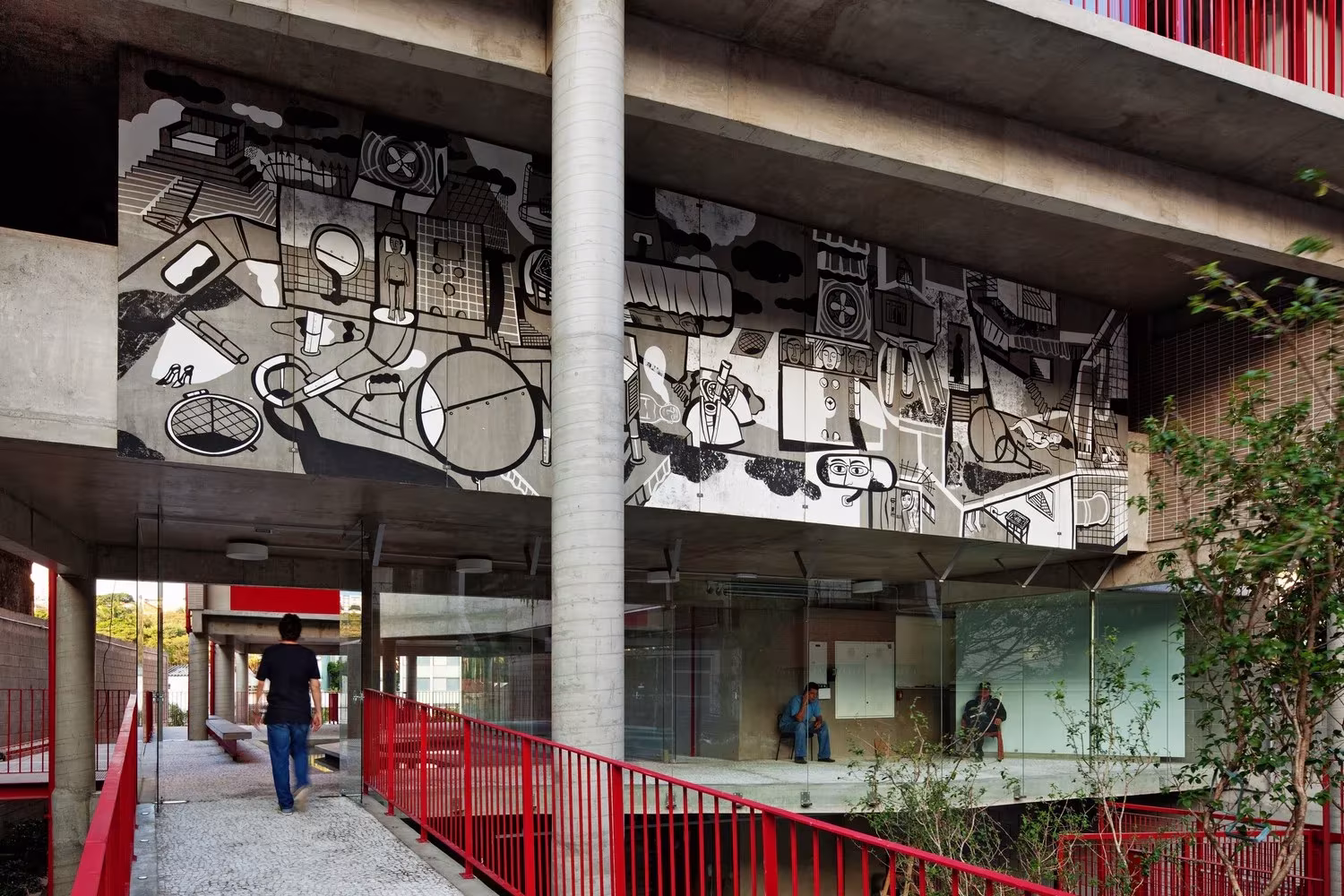 Peatón en el paso bajo el mural en blanco y negro del edificio de Grupo SP, entre pilares de hormigón y vegetación