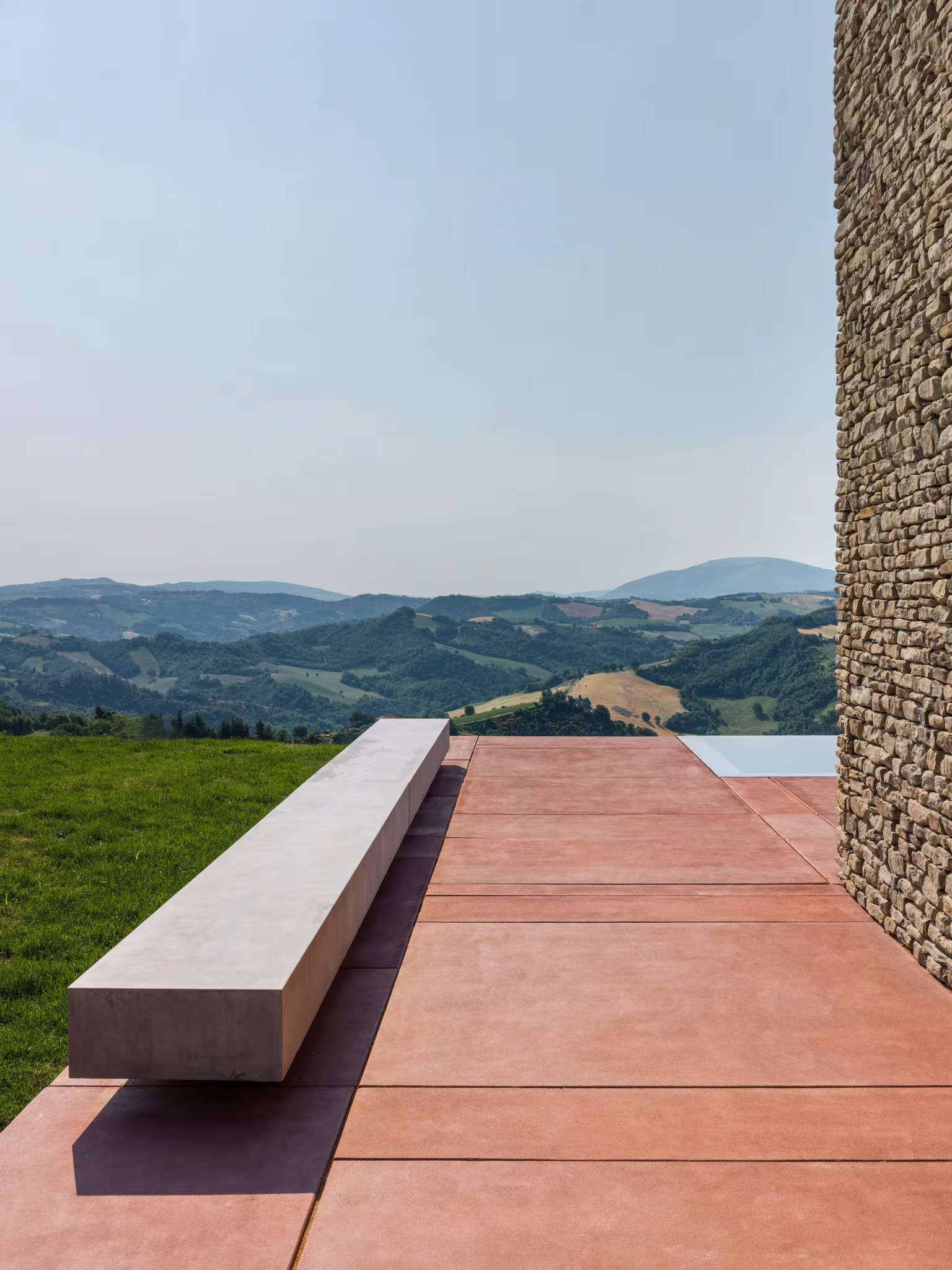 Banco de hormigón sobre la terraza roja de la AP House de GGA Architects frente a los Apeninos