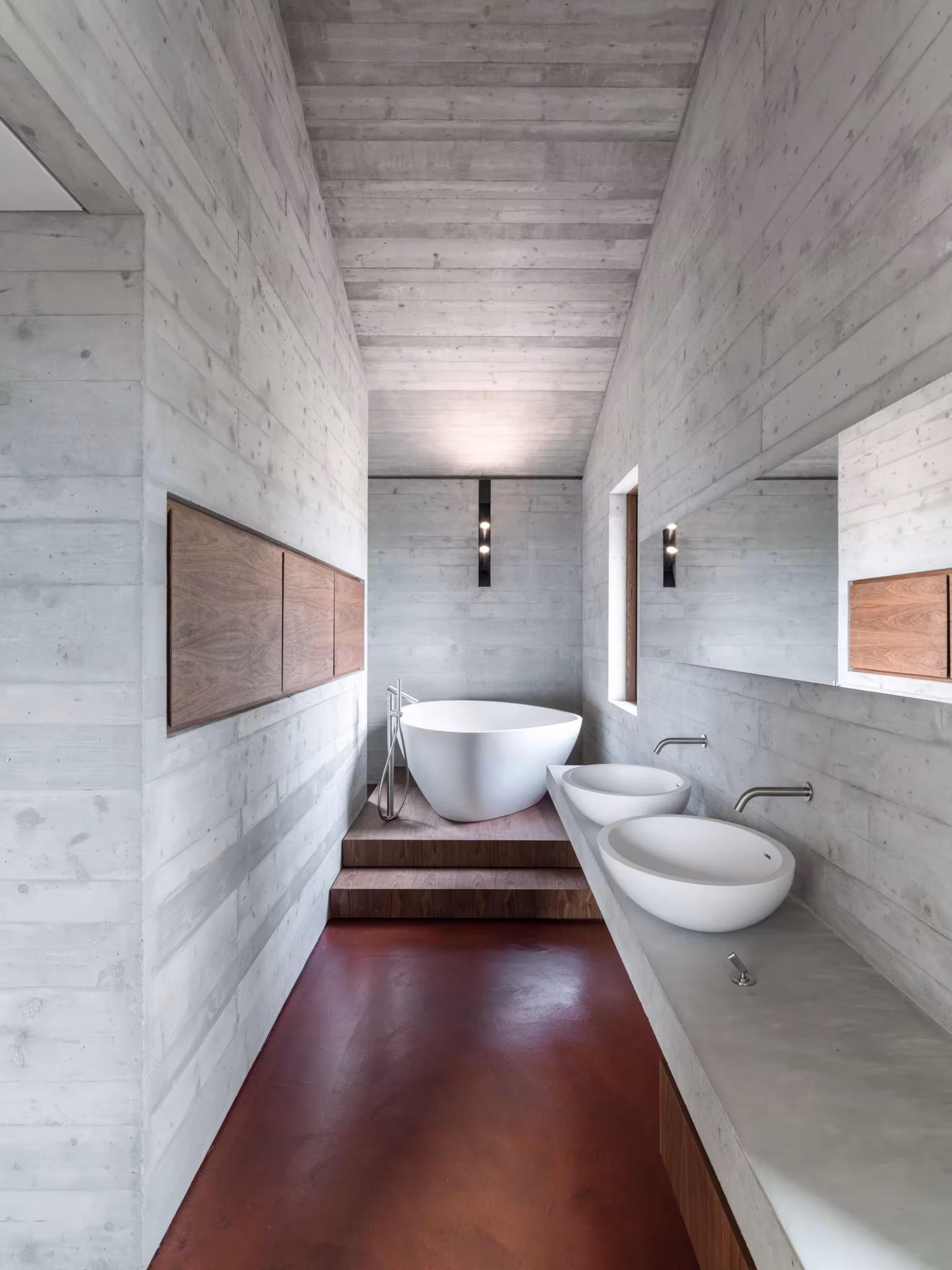 Baño de hormigón visto con bañera exenta, lavabos de piedra y paneles de madera en la AP House de Urbino