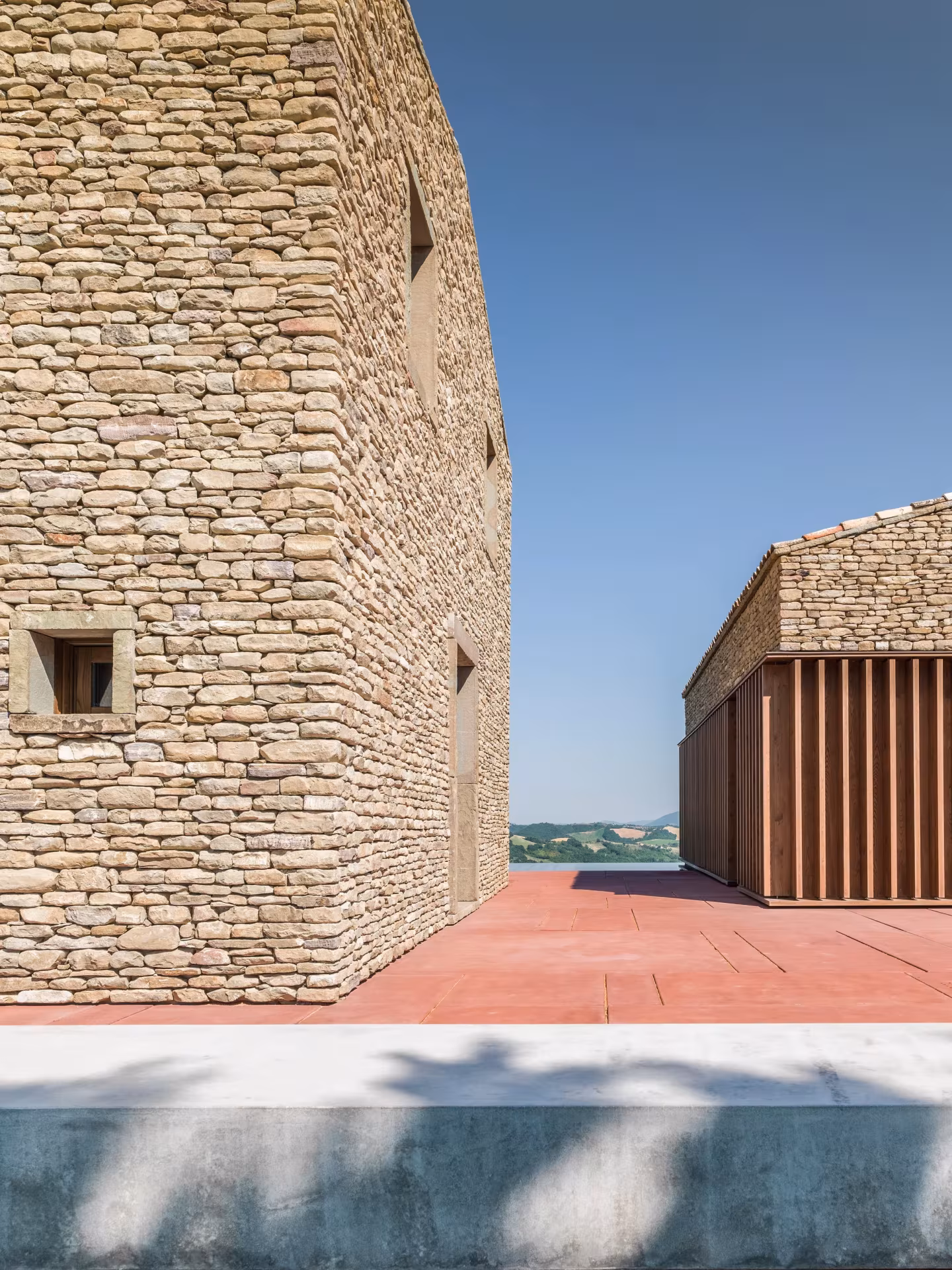 Torre de mampostería y terraza de hormigón rojo de la AP House con vistas abiertas a las colinas de Urbino