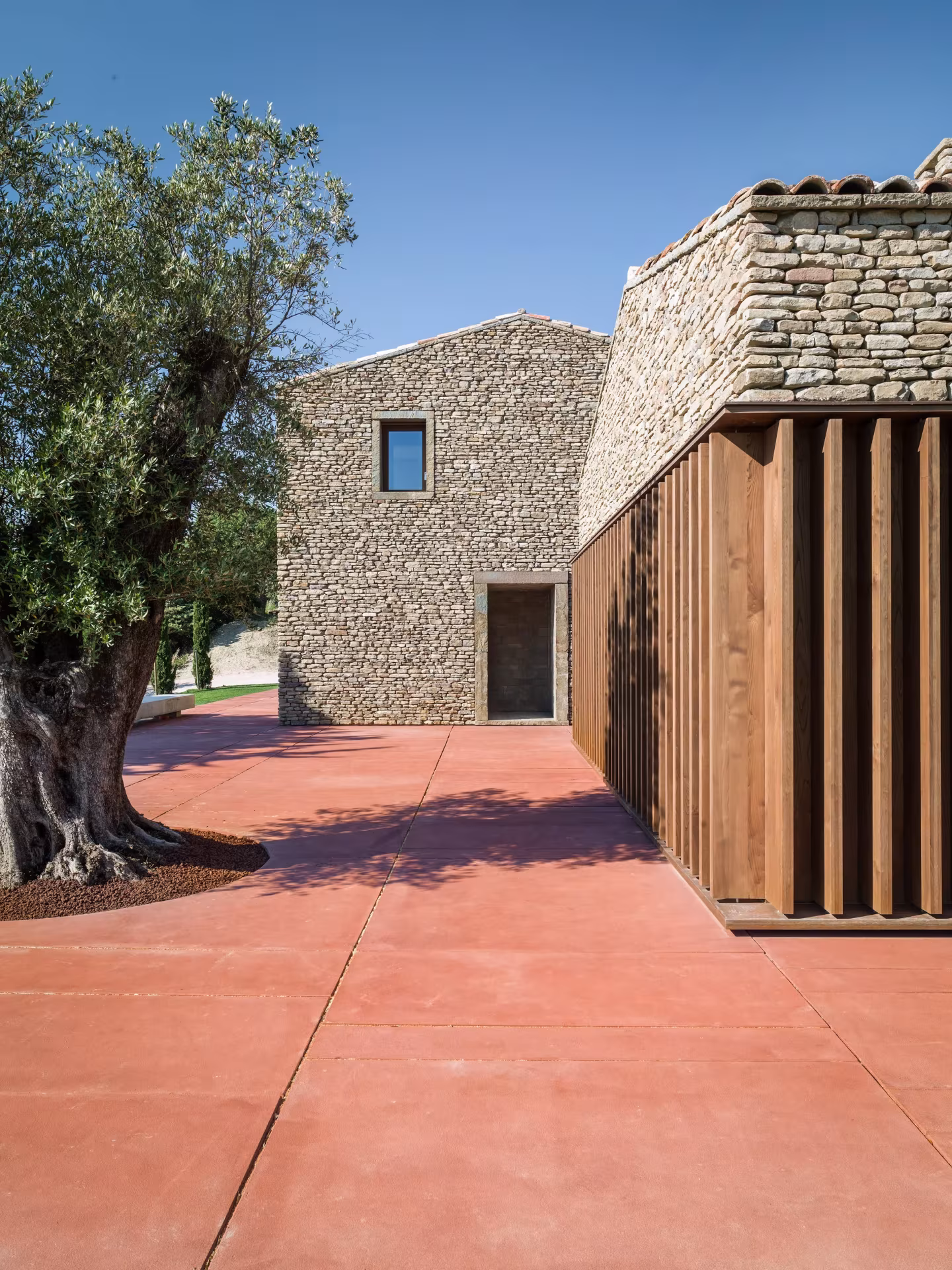 Fachada de piedra y celosía de madera de la AP House de GGA Architects junto a un olivo en Urbino