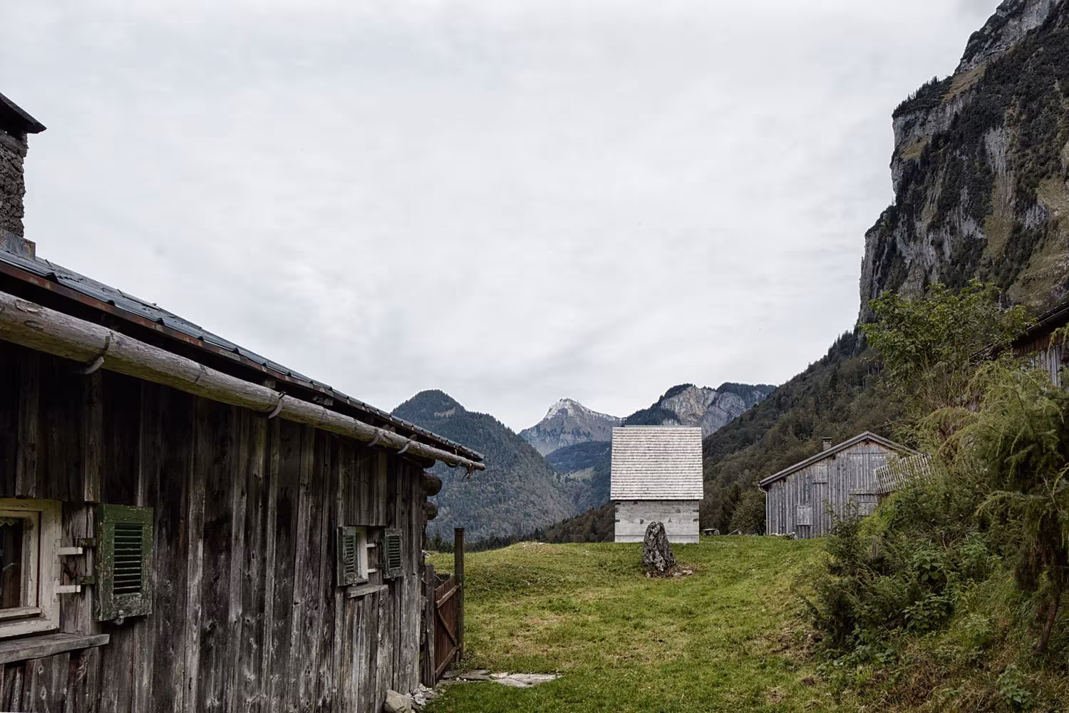 Capilla de hormigón de Wirmboden junto a una casa de madera y bajo un risco en el valle alpino de Vorarlberg