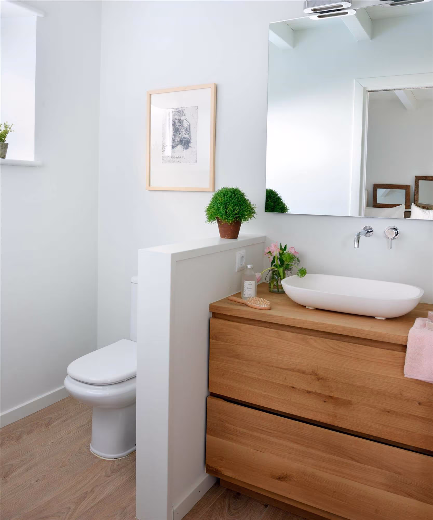 Baño blanco con mueble de madera clara, lavabo sobre encimera, plantas verdes y espejo amplio