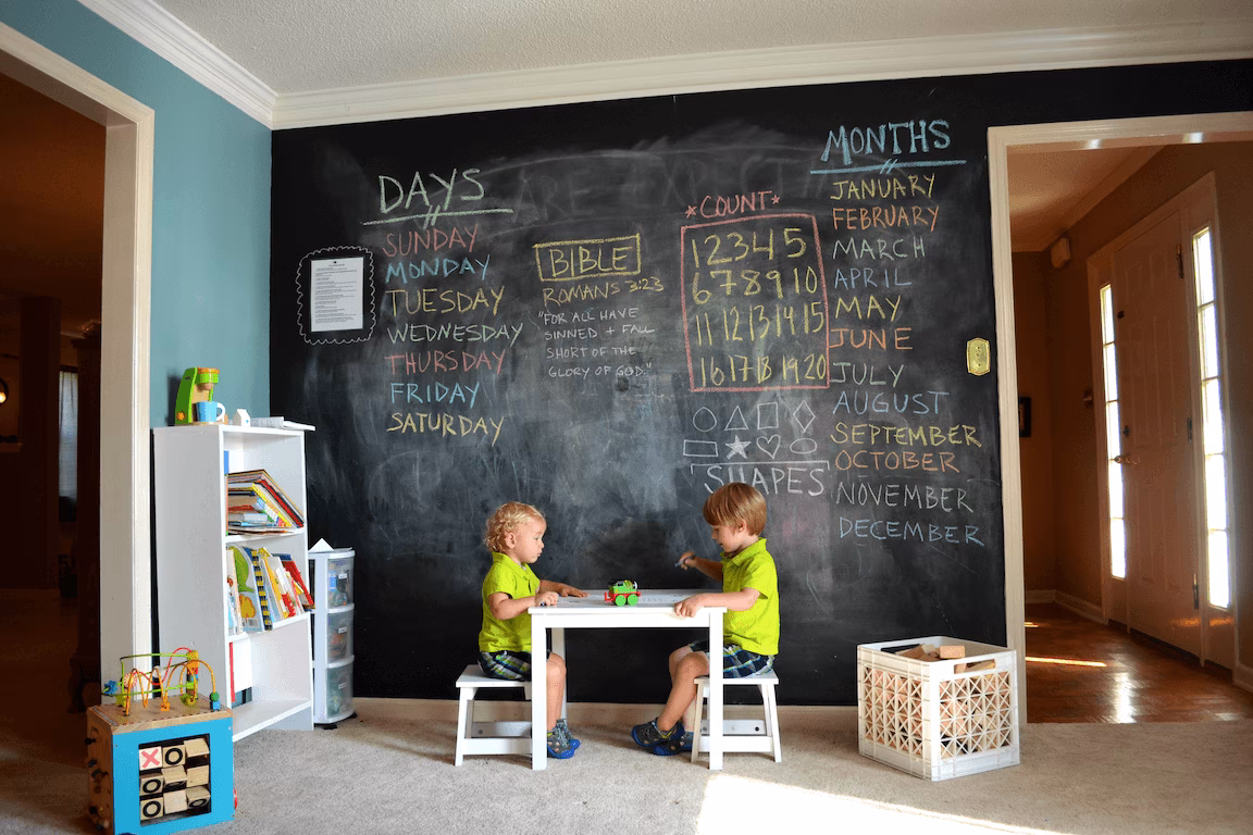 Dos niños jugando junto a una gran pared de pizarra con anotaciones en una habitación de paredes azules