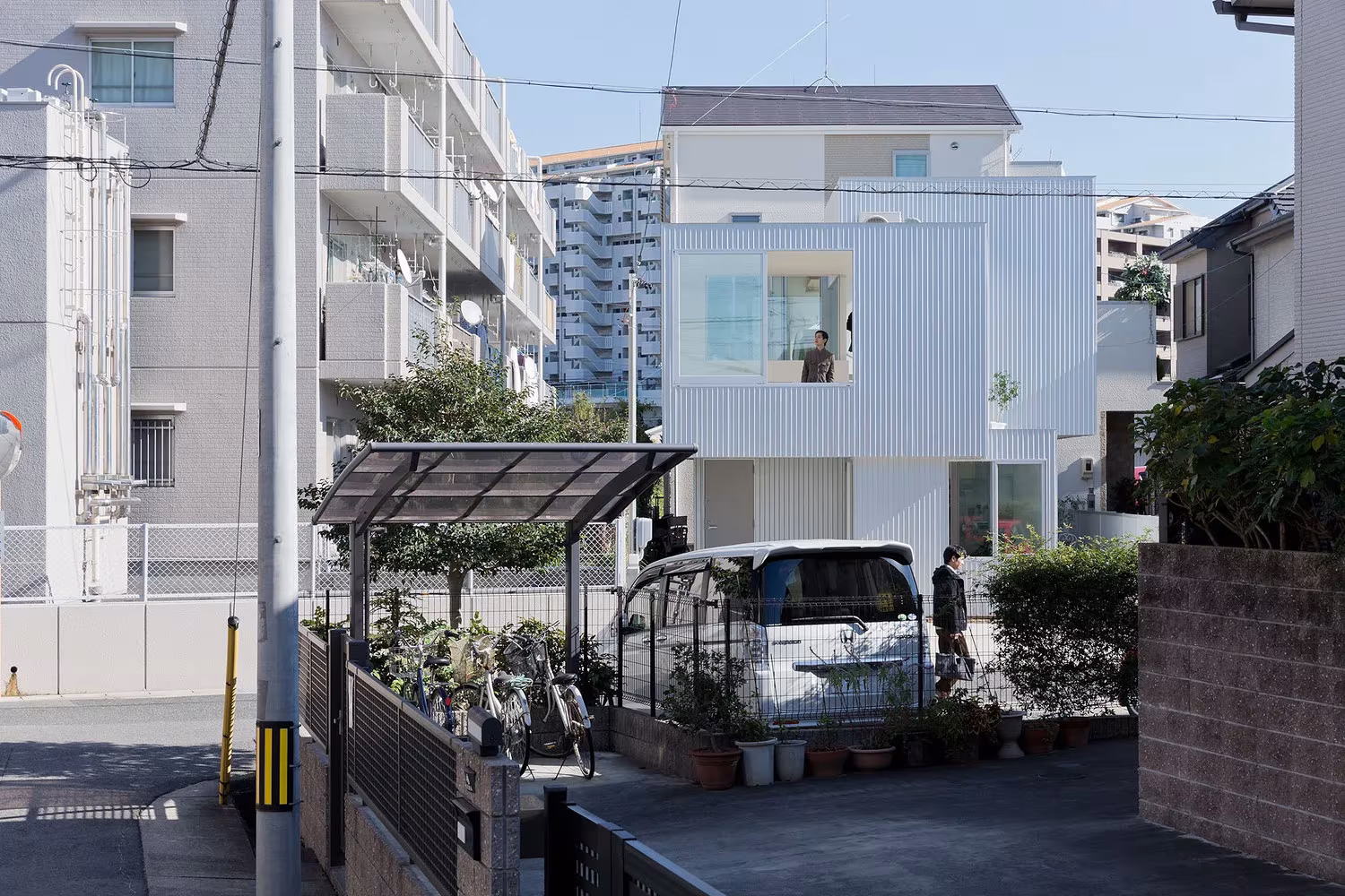 Fachada de chapa blanca de la Casa Chayagasaka vista desde la calle, con pérgola y furgoneta en primer plano, Nagoya