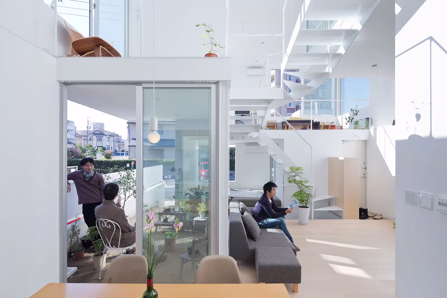 Sala de estar con sofá y mesa de comedor en la Casa Chayagasaka, con la escalera blanca al fondo, Nagoya