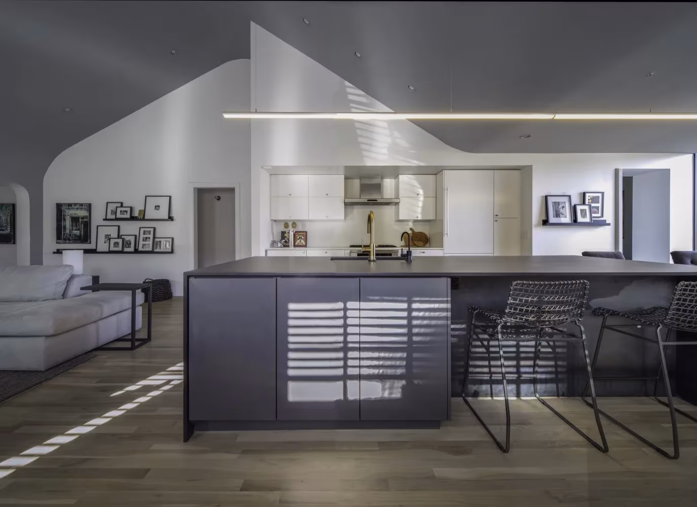 Cocina con isla oscura y taburetes de rejilla bajo un techo blanco de perfil quebrado en la Renovación Escobar