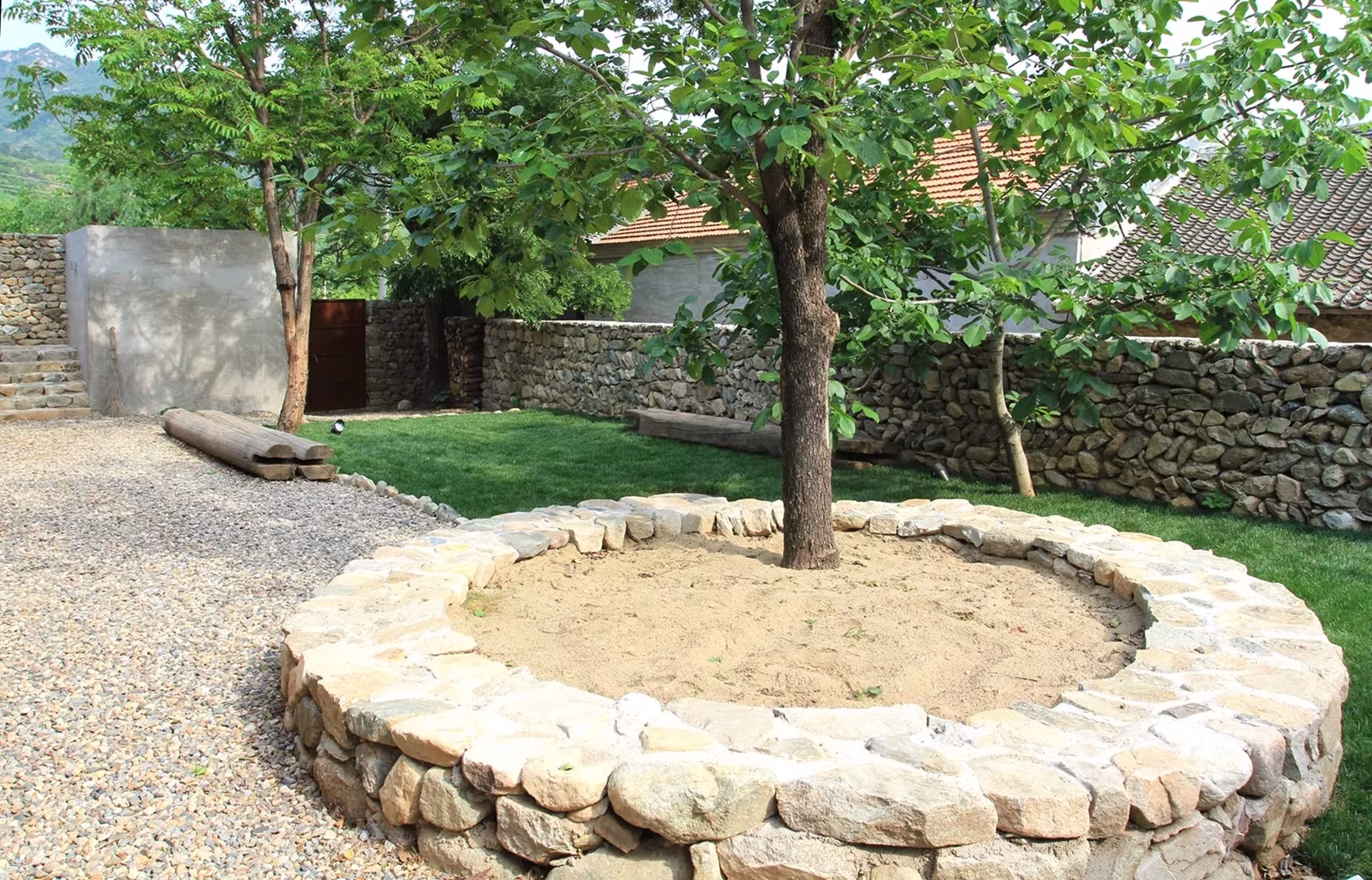 Alcorque circular de piedra en torno a un árbol sobre césped y grava en el patio del Studio Cottage de Clou Architects